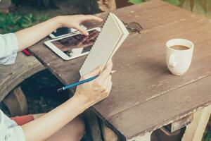 mano mujer utilizando tableta y participación cuaderno en mesa madera a café tienda. foto