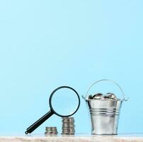 A stack of metal coins and a plastic magnifier on a blue background. The concept of increasing taxes, subsidies photo