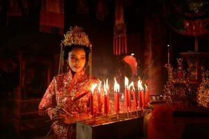 chino mujer hacer deseos, orar, y ligero velas en el ocasión de el anual chino nuevo año festival, en un venerado santuario o templo foto