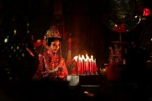 chino mujer hacer deseos, orar, y ligero velas en el ocasión de el anual chino nuevo año festival, en un venerado santuario o templo foto