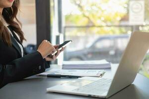 Asian businesswoman in black suit using a mobile phone to communicate with customers to report life insurance expenses and recording uncle's laptop inside office health insurance concept photo