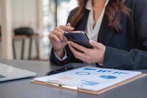 Asian businesswoman in black suit using a mobile phone to communicate with customers to report life insurance expenses and recording uncle's laptop inside office health insurance concept photo