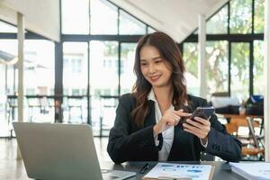 Asian businesswoman in black suit using a mobile phone to communicate with customers to report life insurance expenses and recording uncle's laptop inside office health insurance concept photo