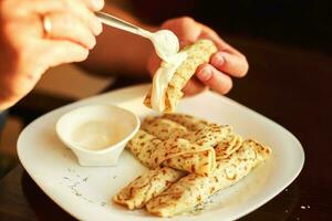 pancakes rolled in a straw on a plate with sour cream. man eating pancake photo