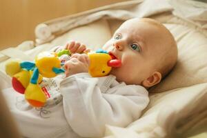 a small child lies and plays with a toy. baby with a toy in his mouth photo