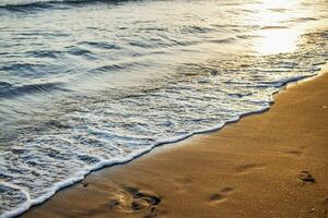 soft sea waves with a foam breaking on a sandy shore tropical beach at summer at sunset photo