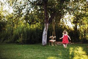 girl in the garden playing with swings. baby playing in the garden alone photo