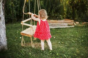 girl in the garden playing with swings. baby playing in the garden alone photo