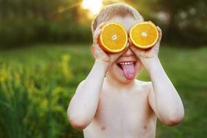 niño con mitades de naranjas en ojos. contento niño teniendo divertido y demostración lengua foto