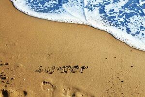 palabra verano escrito en el arenoso playa y huella con ola y Copiar espacio foto