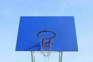 Blue basketball backboard with old and broken net against blue sky background. photo