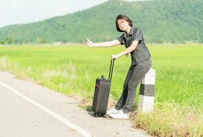 Woman short hair with luggage hitchhiking and thumbs up photo