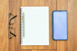Top view image of open notebook with blank page and cellphone on wooden table photo