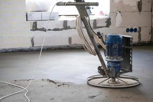 Ramming and grinding of semi-dry floor screed by a machine with a rotating disk for leveling. Construction of a concrete floor in the house, a master with special equipment. photo