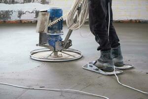 Ramming and grinding of semi-dry floor screed by a machine with a rotating disk for leveling. Construction of a concrete floor in the house, a master with special equipment. photo