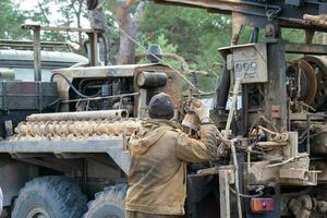 Team of workers with drilling rig on car are drilling artesian well for water in ground. Insertion of metal casing pipe into ground, installation of individual drinking supply, June 28, 2022, Russia, photo