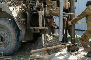 Team of workers with drilling rig on car are drilling artesian well for water in ground. Insertion of metal casing pipe into ground, installation of individual drinking supply, June 28, 2022, Russia, photo