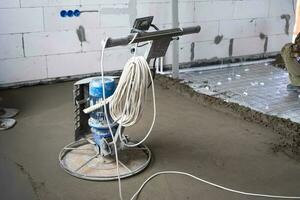 Ramming and grinding of semi-dry floor screed by a machine with a rotating disk for leveling. Construction of a concrete floor in the house, a master with special equipment. photo