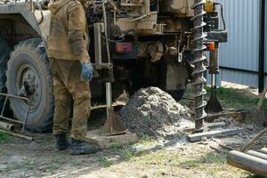 Team of workers with drilling rig on car are drilling artesian well for water in ground. Insertion of metal casing pipe into ground, installation of individual drinking supply, June 28, 2022, Russia, photo