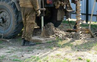 Team of workers with drilling rig on car are drilling artesian well for water in ground. Insertion of metal casing pipe into ground, installation of individual drinking supply, June 28, 2022, Russia, photo