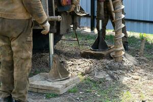 Team of workers with drilling rig on car are drilling artesian well for water in ground. Insertion of metal casing pipe into ground, installation of individual drinking supply, June 28, 2022, Russia, photo