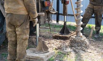 Team of workers with drilling rig on car are drilling artesian well for water in ground. Insertion of metal casing pipe into ground, installation of individual drinking supply, June 28, 2022, Russia, photo