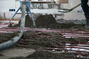 Semi-dry floor screed - a worker shovels a construction mixture through a special sleeve for cementing and leveling on underfloor heating pipes. photo