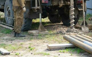 Team of workers with drilling rig on car are drilling artesian well for water in ground. Insertion of metal casing pipe into ground, installation of individual drinking supply, June 28, 2022, Russia, photo