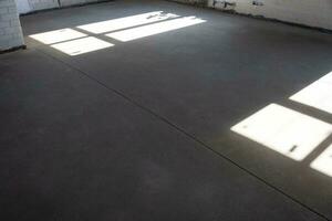 The leveled rough floor in a house under construction with a semi-dry cement screed is a smooth surface with light from the windows photo