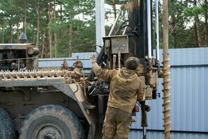 Team of workers with drilling rig on car are drilling artesian well for water in ground. Insertion of metal casing pipe into ground, installation of individual drinking supply, June 28, 2022, Russia, photo