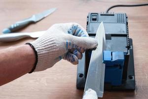 Sharpening a knife on an electric sharpener at home. The man's hand drives the knife blade between the blue sharpeners, dust flies on the machine. photo