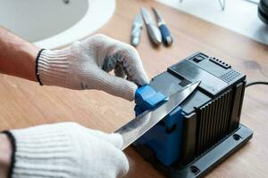 Sharpening a knife on an electric sharpener at home. The man's hand drives the knife blade between the blue sharpeners, dust flies on the machine. photo