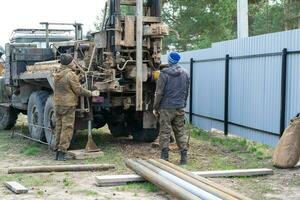 equipo de trabajadores con perforación plataforma en coche son perforación artesiano bien para agua en suelo. inserción de metal caja tubo dentro suelo, instalación de individual Bebiendo suministrar, junio 28, 2022, Rusia, foto