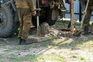 Team of workers with drilling rig on car are drilling artesian well for water in ground. Insertion of metal casing pipe into ground, installation of individual drinking supply, June 28, 2022, Russia, photo