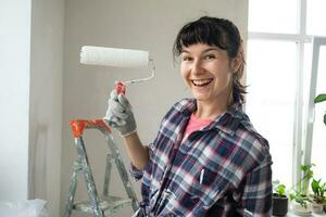Happy woman in paint roller and white paint for walls in hands close-up portrait. Construction work and cosmetic repairs in house, wall painting, tinting, finishing work with your own hands photo