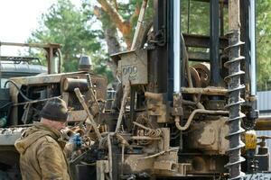 Team of workers with drilling rig on car are drilling artesian well for water in ground. Insertion of metal casing pipe into ground, installation of individual drinking supply, June 28, 2022, Russia, photo