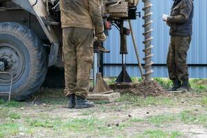 Team of workers with drilling rig on car are drilling artesian well for water in ground. Insertion of metal casing pipe into ground, installation of individual drinking supply, June 28, 2022, Russia, photo