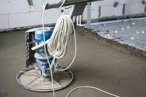 Ramming and grinding of semi-dry floor screed by a machine with a rotating disk for leveling. Construction of a concrete floor in the house, a master with special equipment. photo