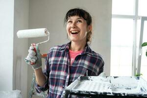 Happy woman in paint roller and white paint for walls in hands close-up portrait. Construction work and cosmetic repairs in house, wall painting, tinting, finishing work with your own hands photo