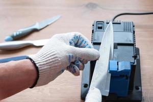 Sharpening a knife on an electric sharpener at home. The man's hand drives the knife blade between the blue sharpeners, dust flies on the machine. photo