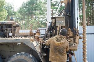 Team of workers with drilling rig on car are drilling artesian well for water in ground. Insertion of metal casing pipe into ground, installation of individual drinking supply, June 28, 2022, Russia, photo