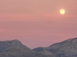 montañas en un noche horizonte con rosado cielo y un amarillo Luna foto