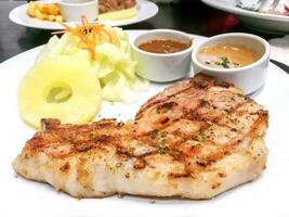 Twin T-bone pork steak with fruit salad,  pepper and tomato sauce on white ceramic plate on black leather table in the restaurant. photo