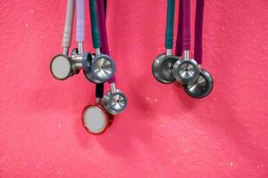 Closeup and crop of Doctor Stethoscopes hanging on pink wall background. photo