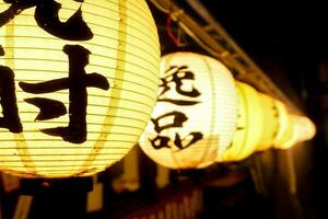 de cerca negro japonés textos en papel linterna colgando debajo japonés restaurante alero en noche tiempo. foto