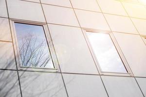 Closeup and crop reflection and shadow of winter tree and bright blue sky on office building windows with sun and lens flare. photo