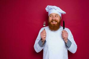 happy chef with beard and red apron holds cutlery in hand photo