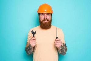 Confused man with screwdriver and spanners. worried and uncertain expression. cyan background photo