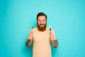 Happy man with tattoos is ready to eat with cutlery in hand photo