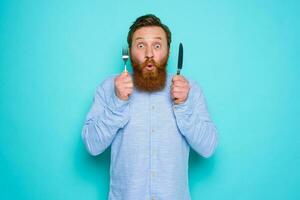 Shocked man with tattoos is ready to eat something with cutlery in hand photo